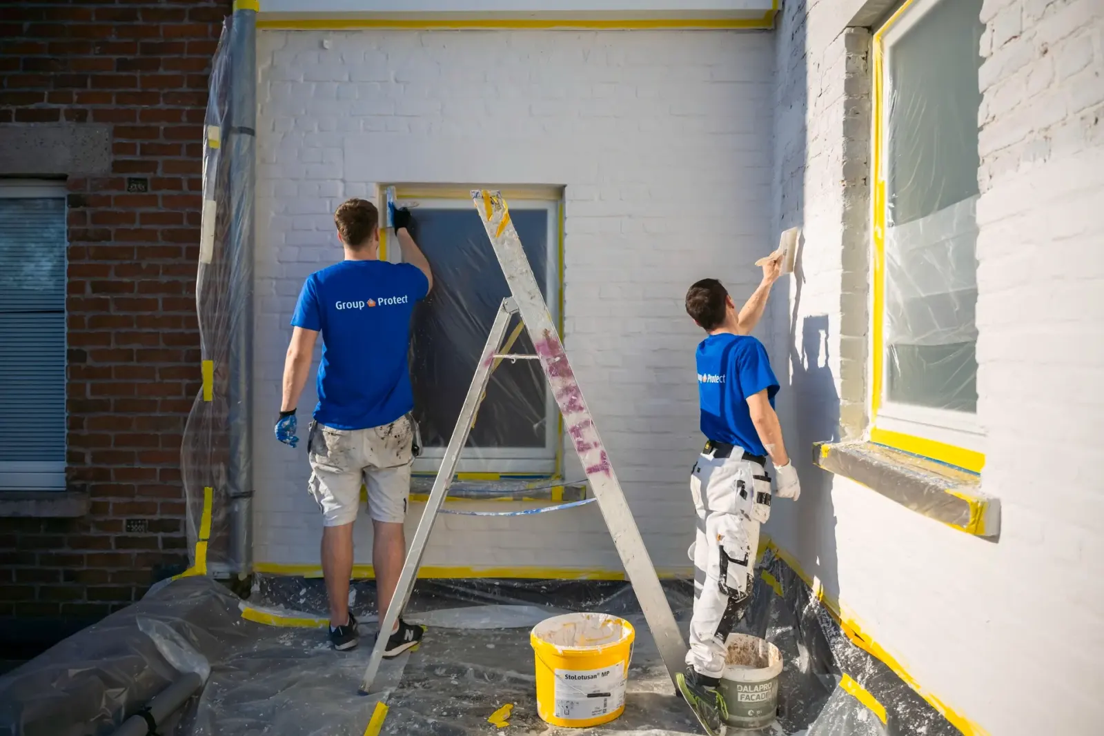 Twee vakmannen van Group Protect brengen witte kalei aan op buitengevel voor duurzame renovatie en energiebesparende afwerking.