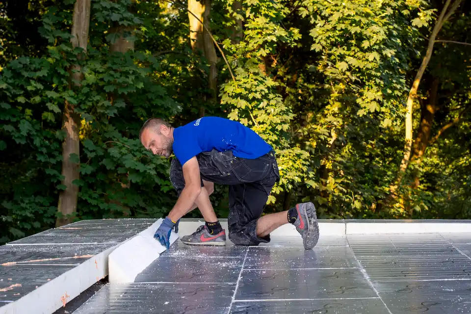 Dakwerker plaatst isolatiepanelen op een plat dak voor betere energie-efficiëntie en duurzame bescherming, met focus op energietransitie.