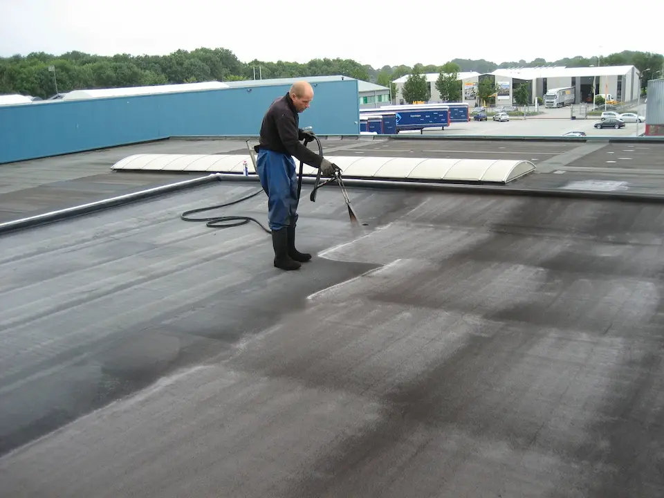 Dakwerker brengt beschermende coating aan op groot plat dak van industrieel gebouw, duurzame waterdichting en isolatie door Energy Protect.