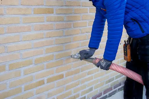 Slang blaast isolatiemateriaal in spouwmuur via boorgat in gevelsteen energiezuinige woningrenovatie door Energy Protect