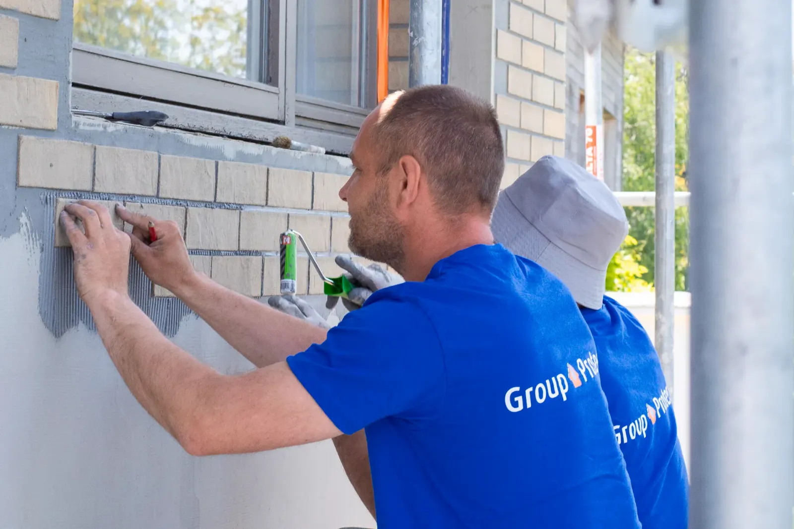 Twee vakmannen plaatsen beige steenstrips rond raamkozijn tijdens duurzame gevelisolatie en renovatie door Energy Protect.