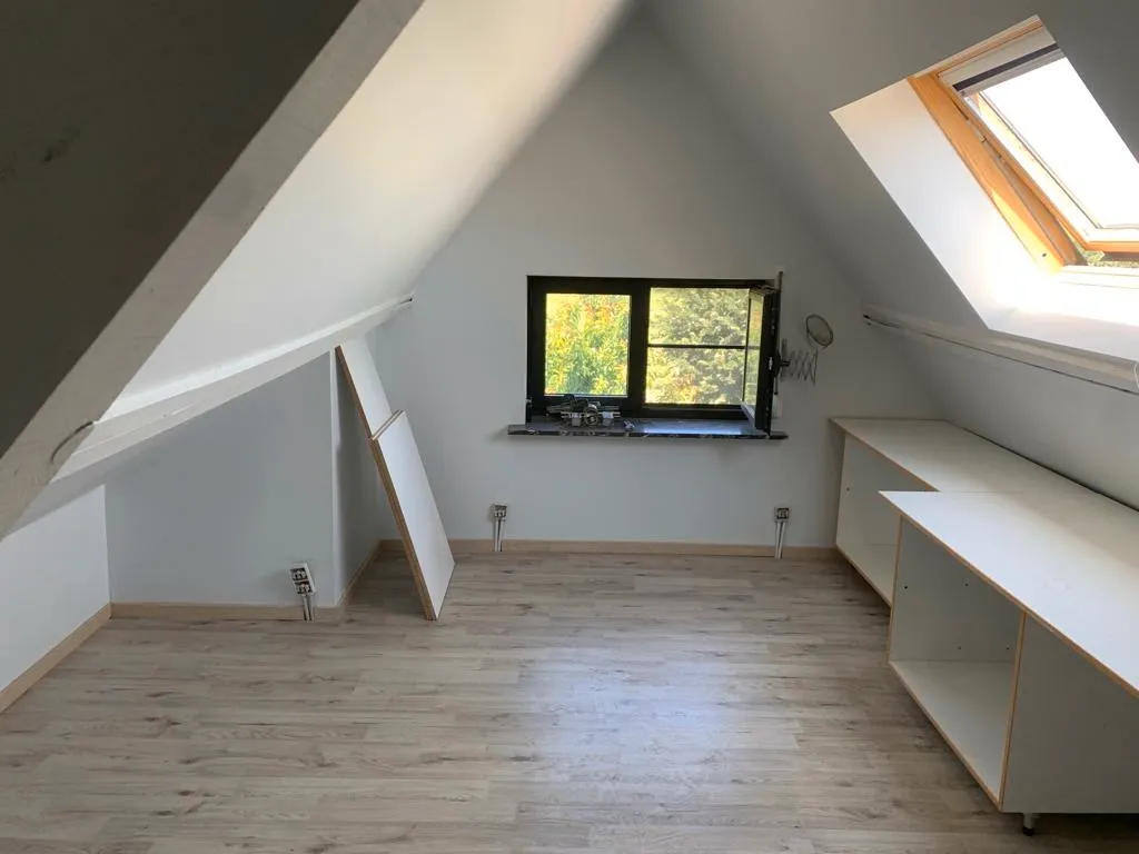 Leeg ruime zolder met houtlook vloer, wit schuine dak en een groot dakraam voor toekomstige isolatie- of renovatiewerkzaamheden