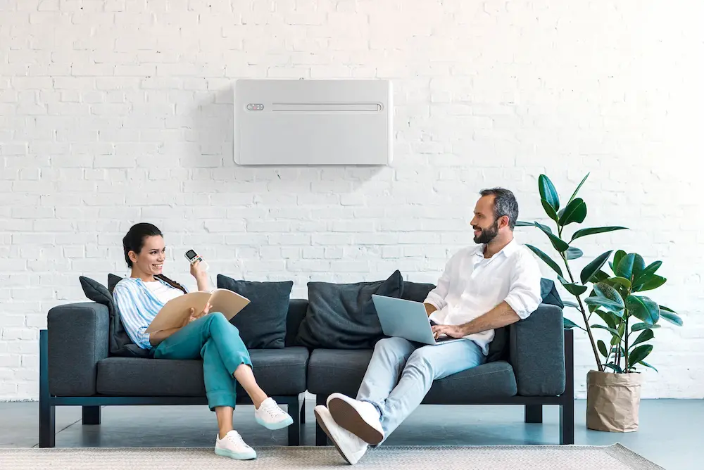 Stijlvolle woonkamer met Energy Protect airco zonder buitenunit, gebruikt door lachend koppel met laptop en afstandsbediening.