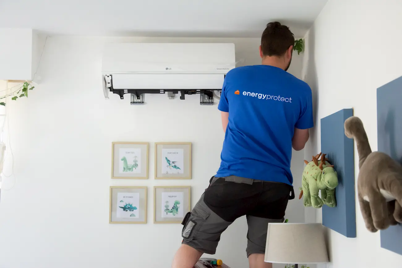 Monteur in blauw Energy Protect T-shirt installeert een LG wandairco in kinderkamer met dinosaurusdecoratie.