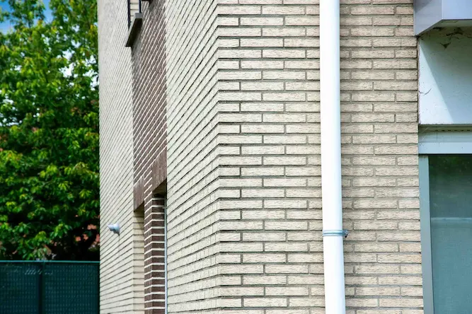 Close-up van gerenoveerde hoekgevel met beige kalei-afwerking en witte regenpijp, uitgevoerd door Energy Protect voor isolatieverbetering.