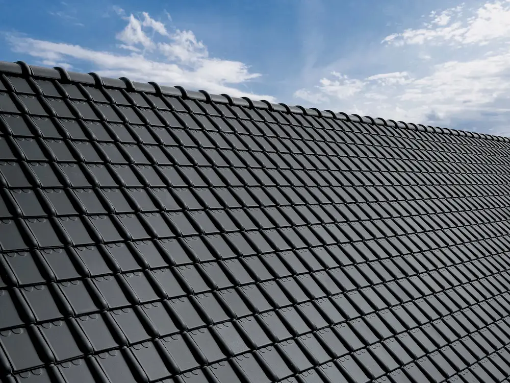 Zwart pannendak met glanzende keramische dakpannen onder blauwe lucht, duurzame dakafwerking voor energie-efficiënte woningen.