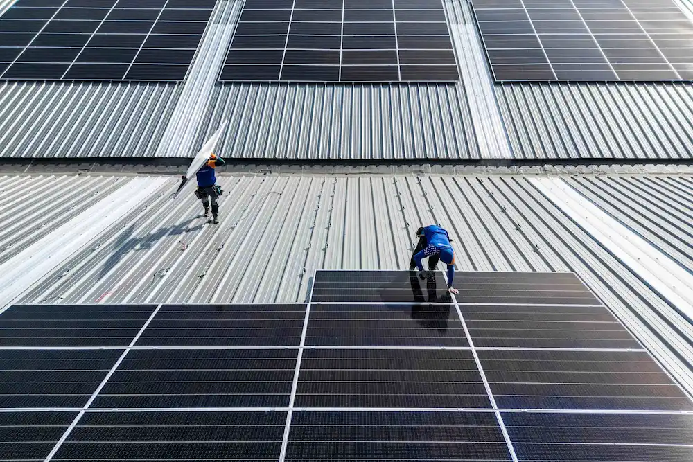 Installateurs van Energy Protect plaatsen zonnepanelen op een groot industrieel golfplaten dak.