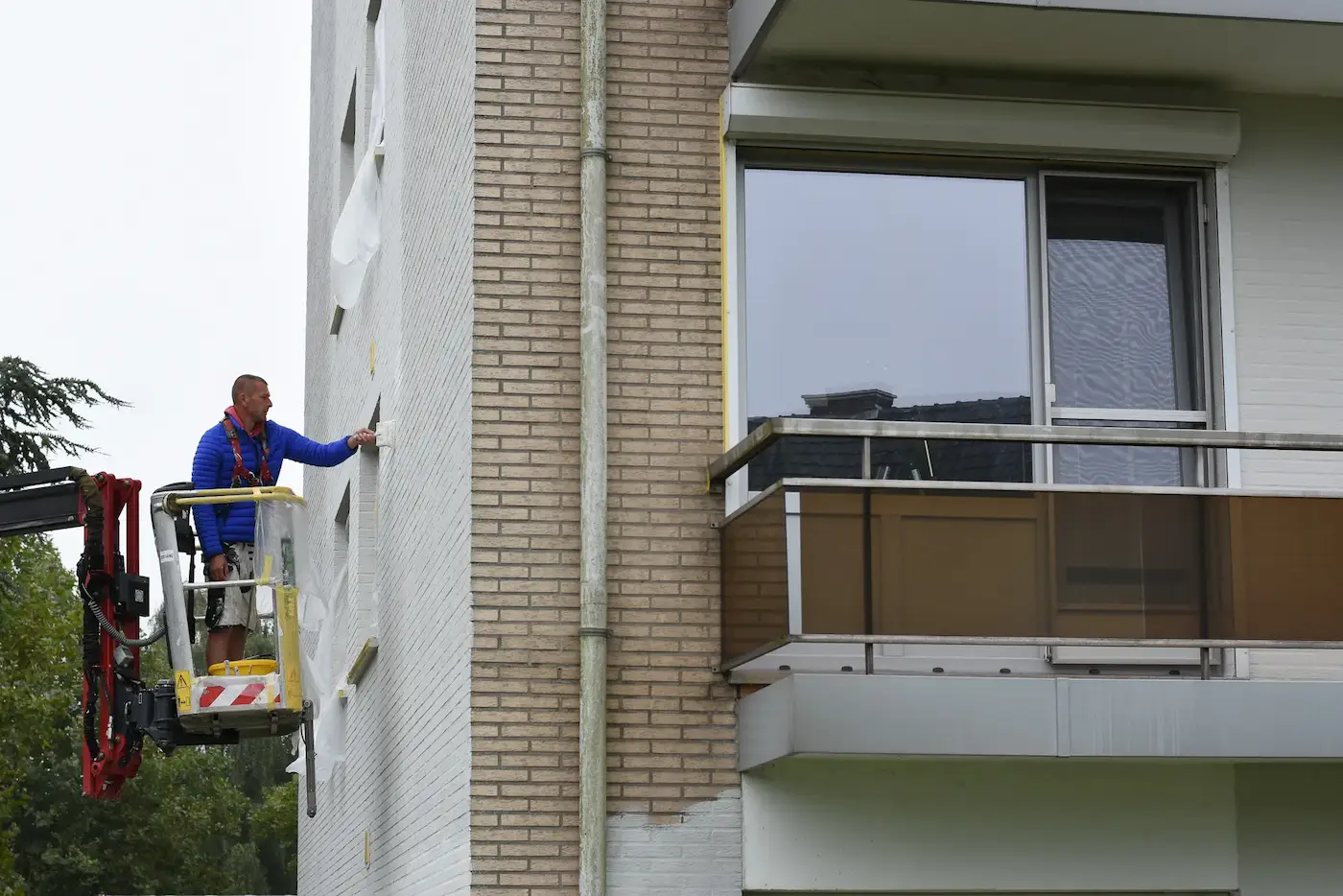 Werknemer van Energy Protect werkt vanuit een hoogwerker aan de gevel van een appartementsgebouw.