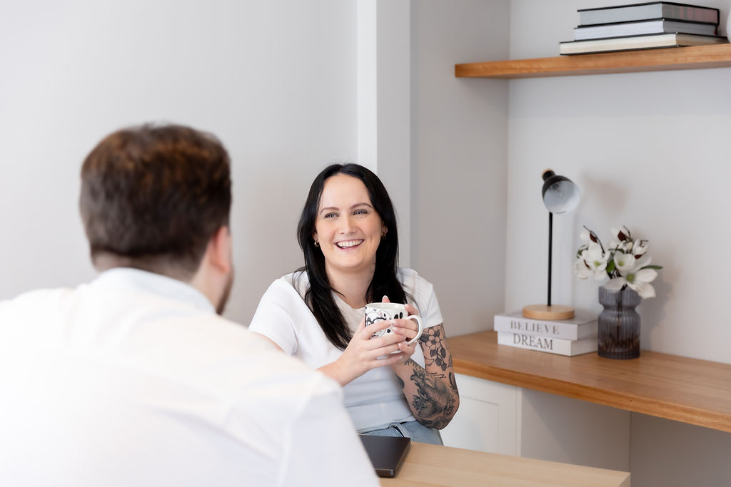 Alice Xerri, Founder and Fractional Content Lead, Freelance Copywriter for Finance, B2B Tech and SaaS, laughing with client at desk drinking a cup of tea.