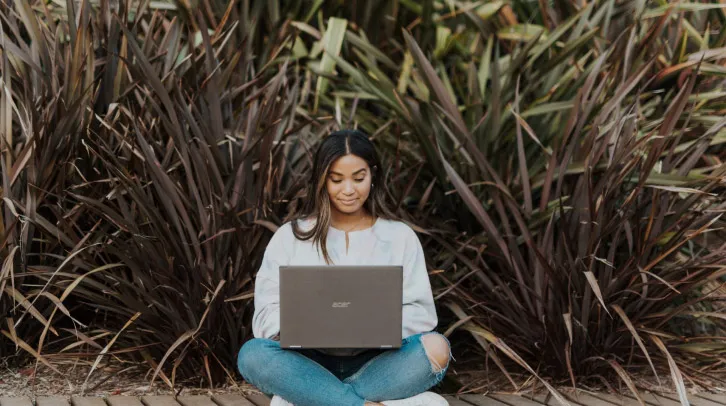 Frau am Laptop vor Grünen Büschen