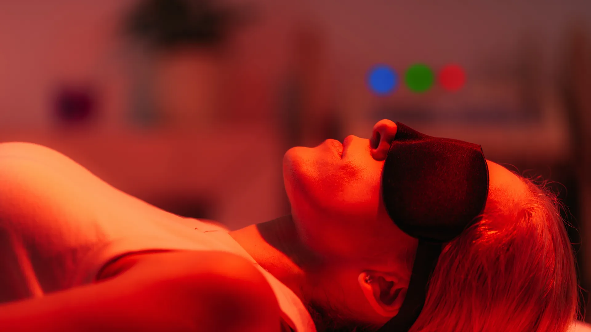 Femme allongée sous lumière rouge lors d’une séance de luminothérapie avec masque de protection.