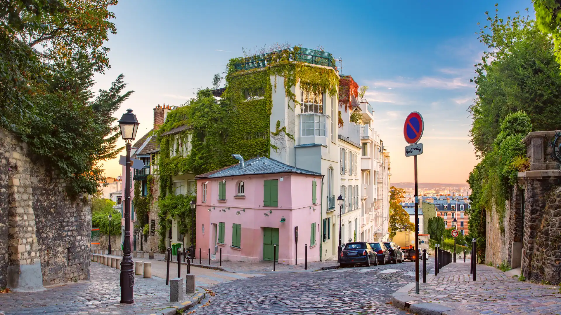 Rue pavée de Montmartre à Paris avec maisons colorées et végétation, au coucher du soleil