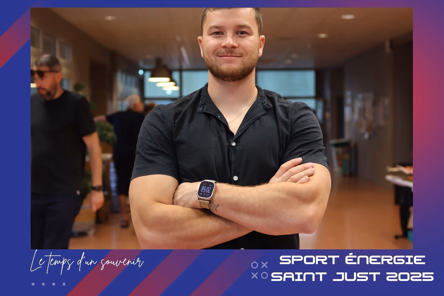 Jeune homme souriant, bras croisés, portant une montre connectée dans un espace intérieur moderne.