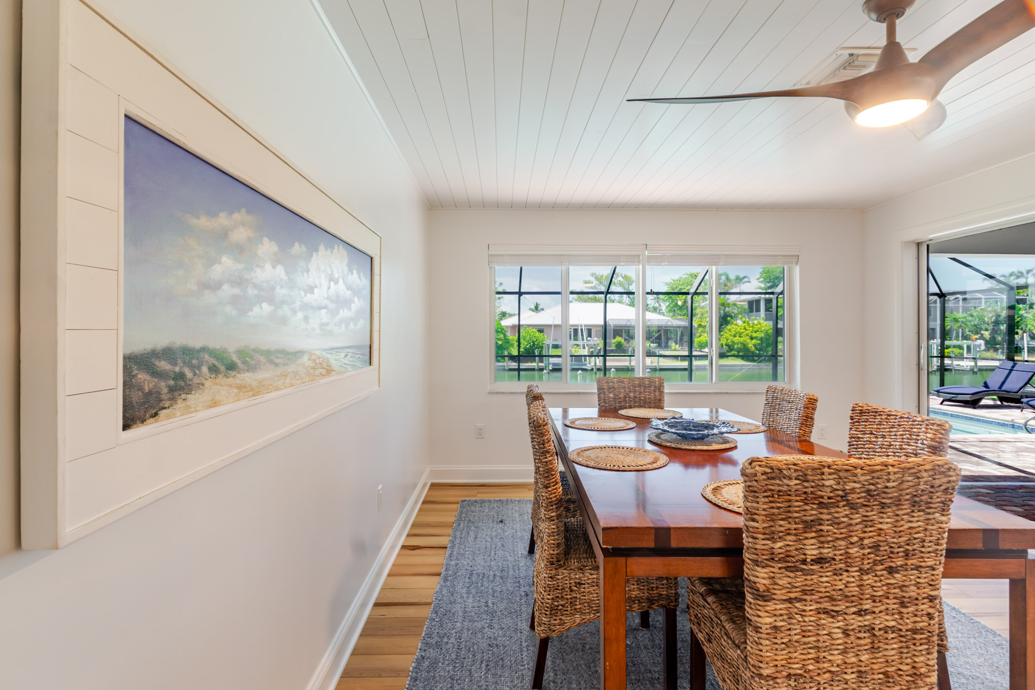 Dining area with coastal art and large windows letting in natural light.