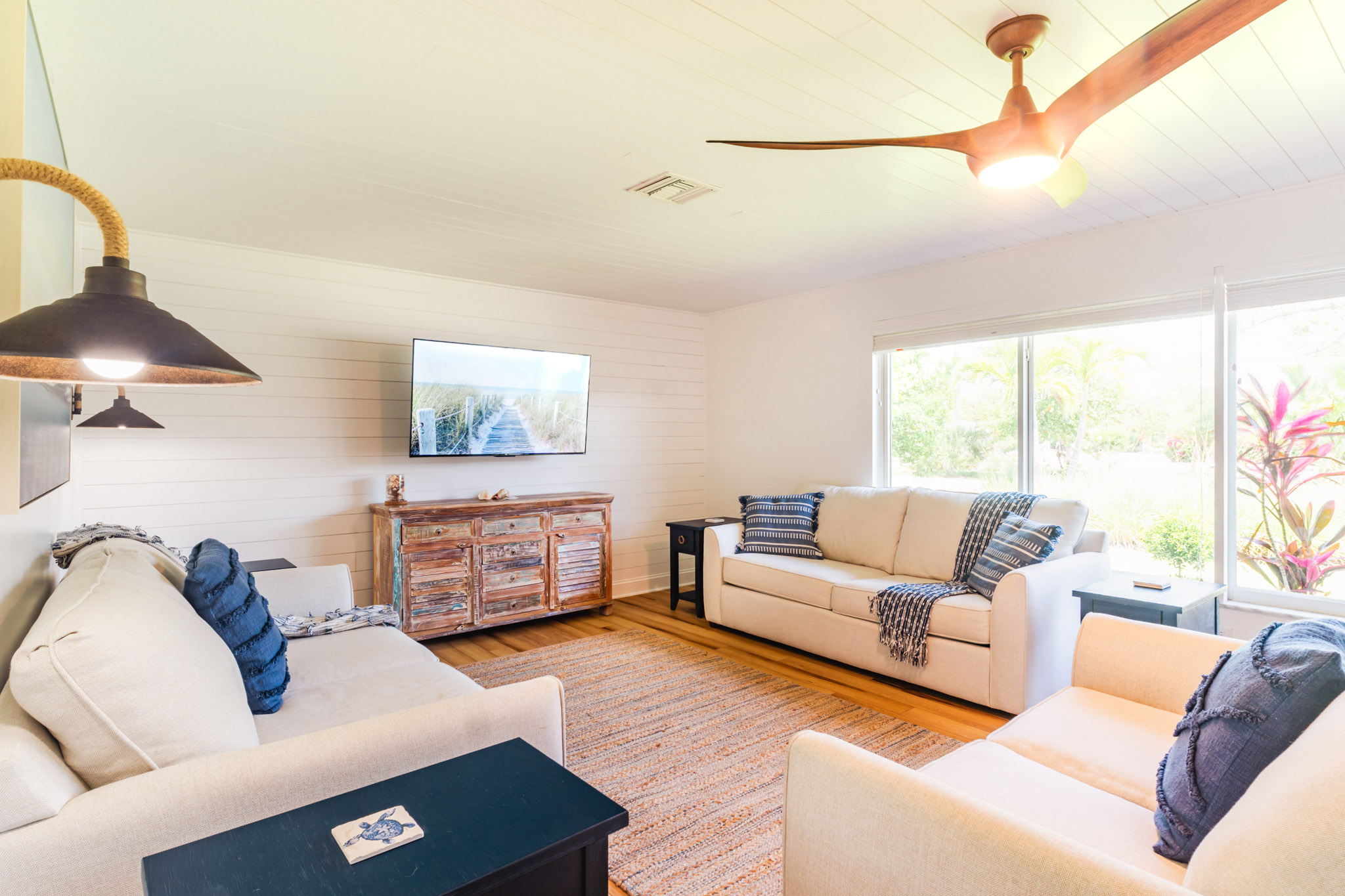 Wide view of the main living room with seating and ceiling fan under natural light.