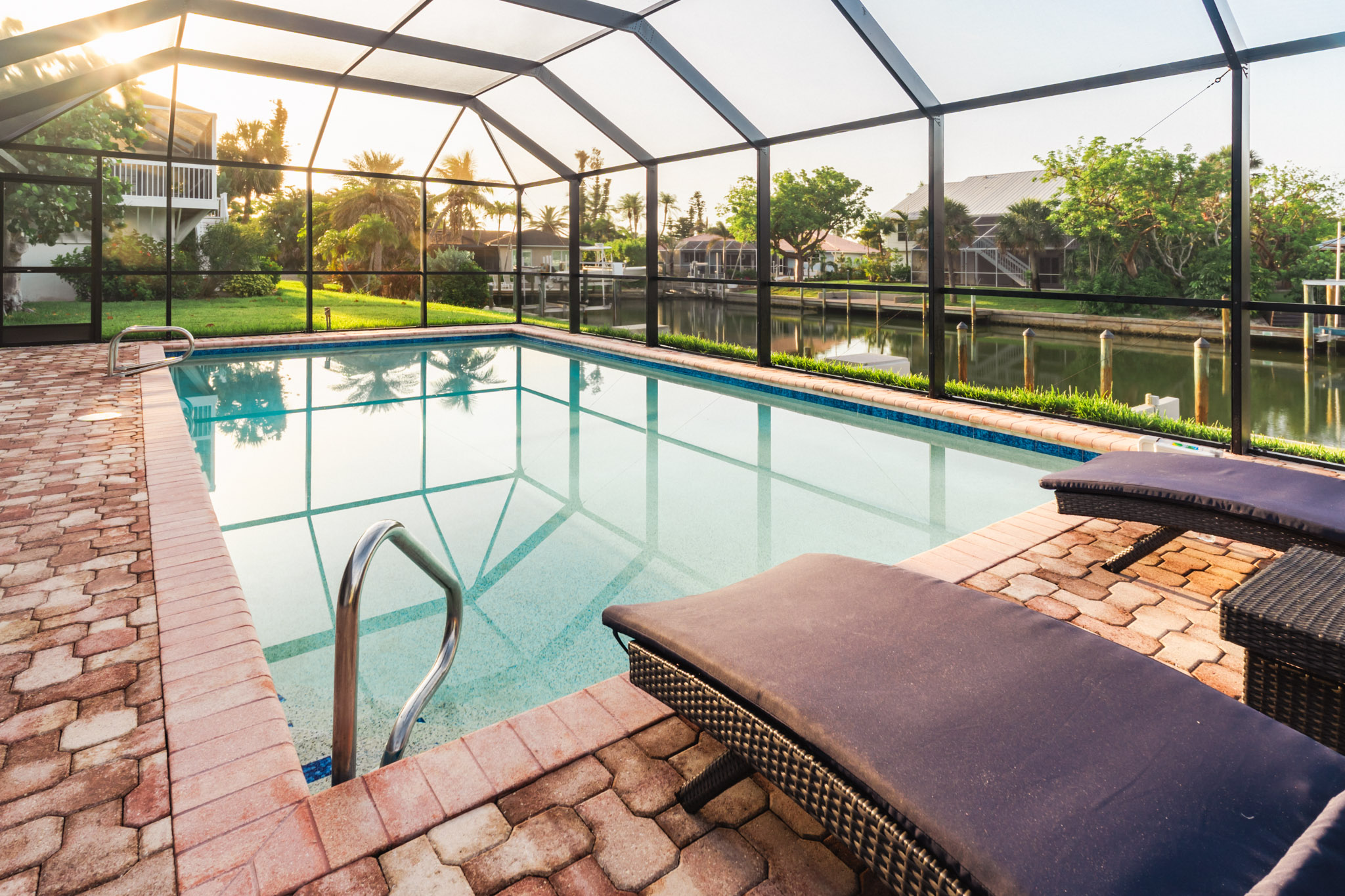Poolside lounge chair beneath screen enclosure with sunrise light.