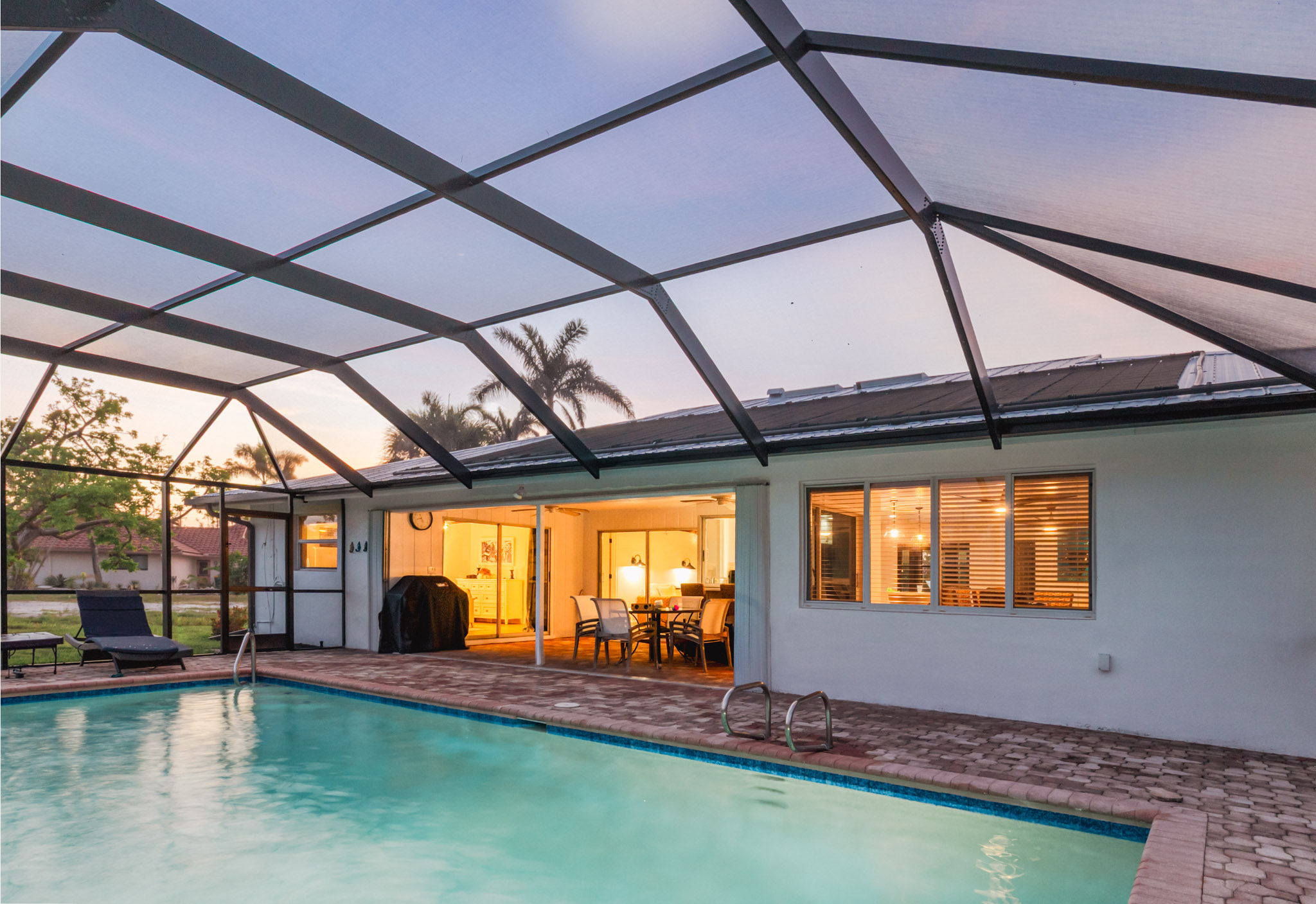 Lanai and Pool evening lit with glowing lights in the windows of the house and pool light
