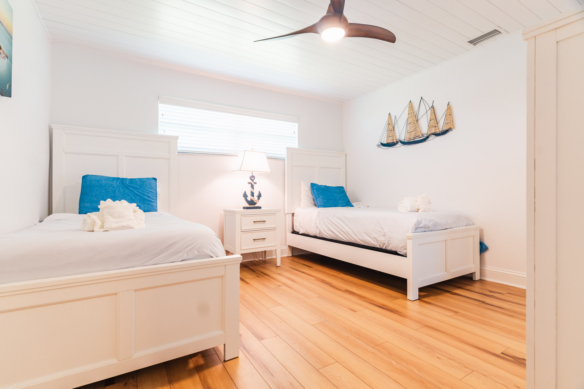 Coastal-inspired twin bedroom in Sanibel vacation home with ceiling fan and soft blue decor.
