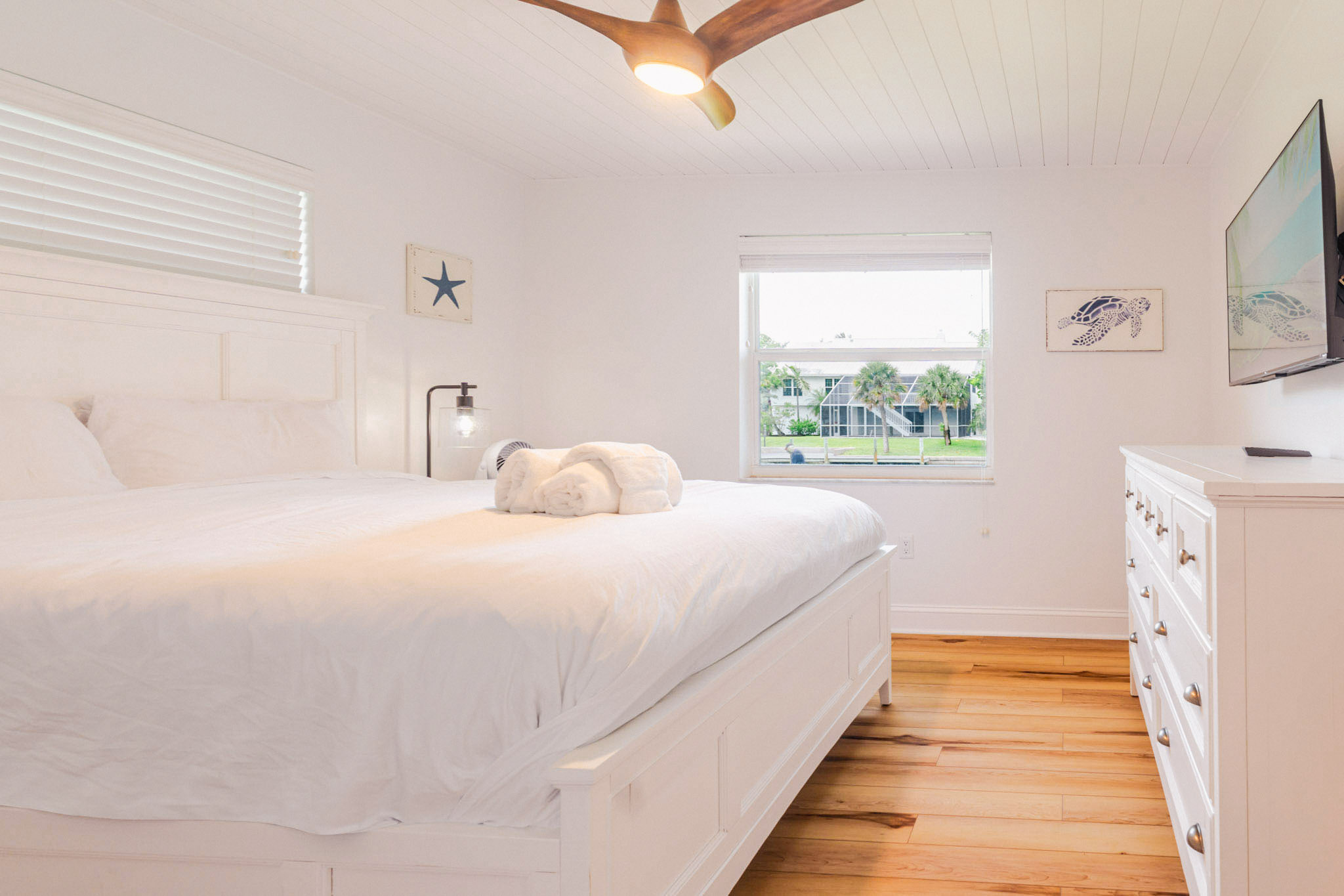 Queen bedroom with sunlit windows, ceiling fan, and elegant white furnishings in a Sanibel Island rental.