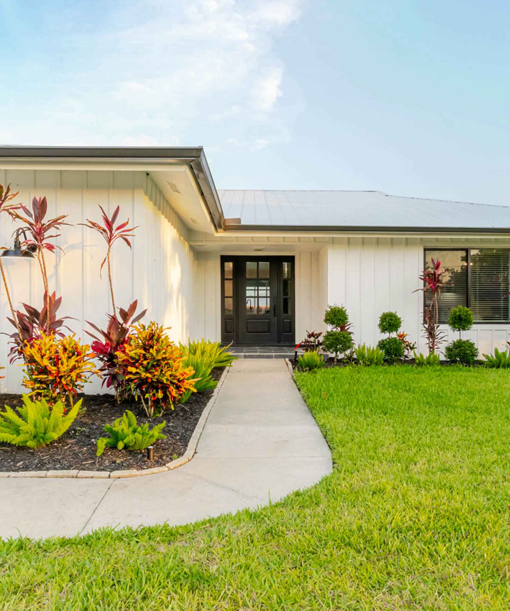 front view of coastal cottage featuring blue skies and manicured lawn and garden 