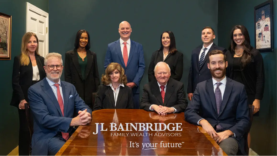 The JL Bainbridge team's group portrait in their boardroom. The JL Bainbridge logo appears over the wooden table toward the bottom of the screen.
