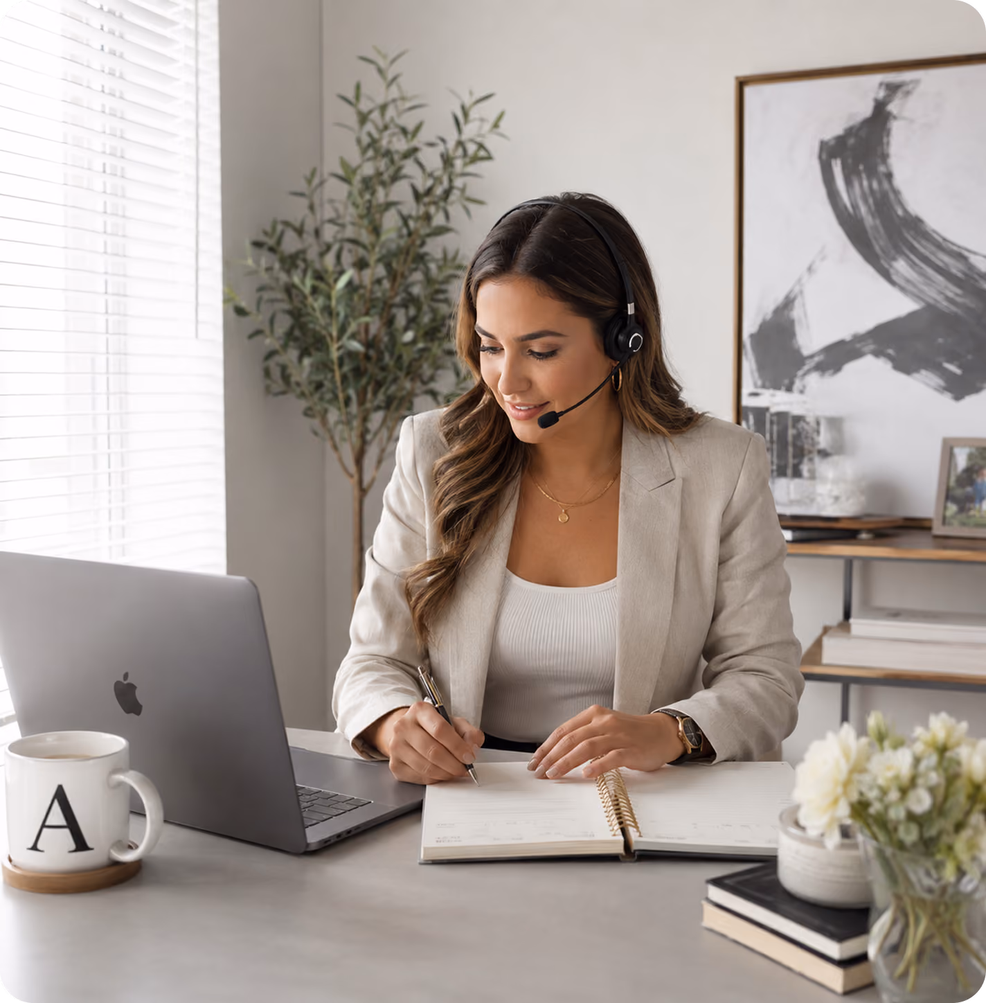 Woman in headset writing in planner while working at laptop in a bright home office.