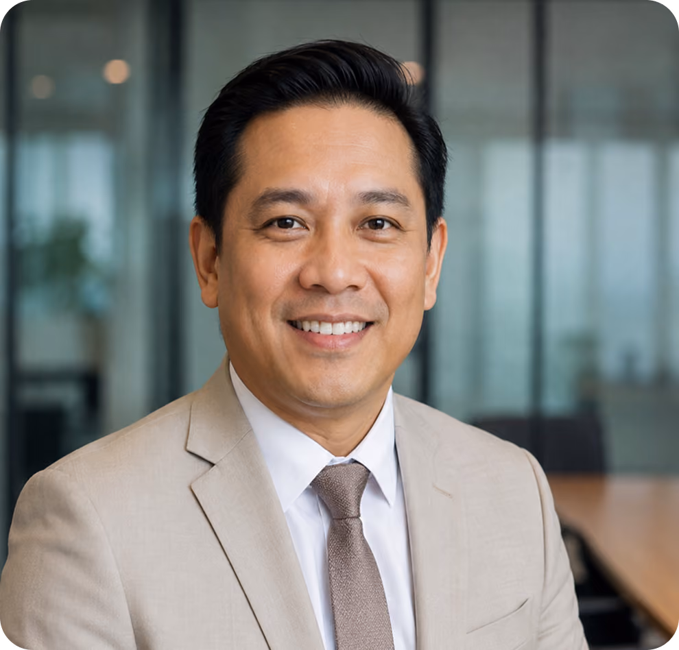 Smiling man in beige suit and tie in an office setting with glass walls and wooden table.