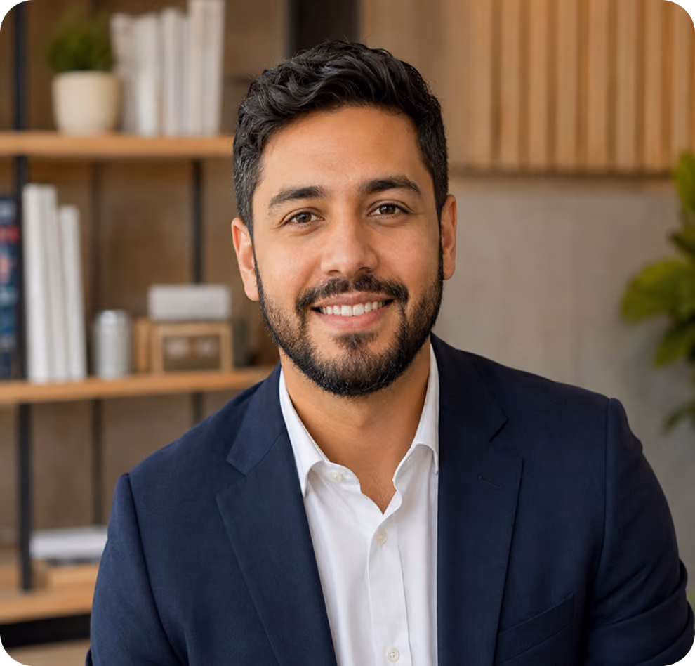 Smiling man with dark hair and beard wearing a navy blazer and white shirt in an office setting.