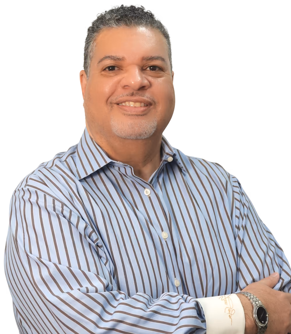 Smiling middle-aged man with short curly hair and light facial hair wearing a blue and white striped button-up shirt with arms crossed.