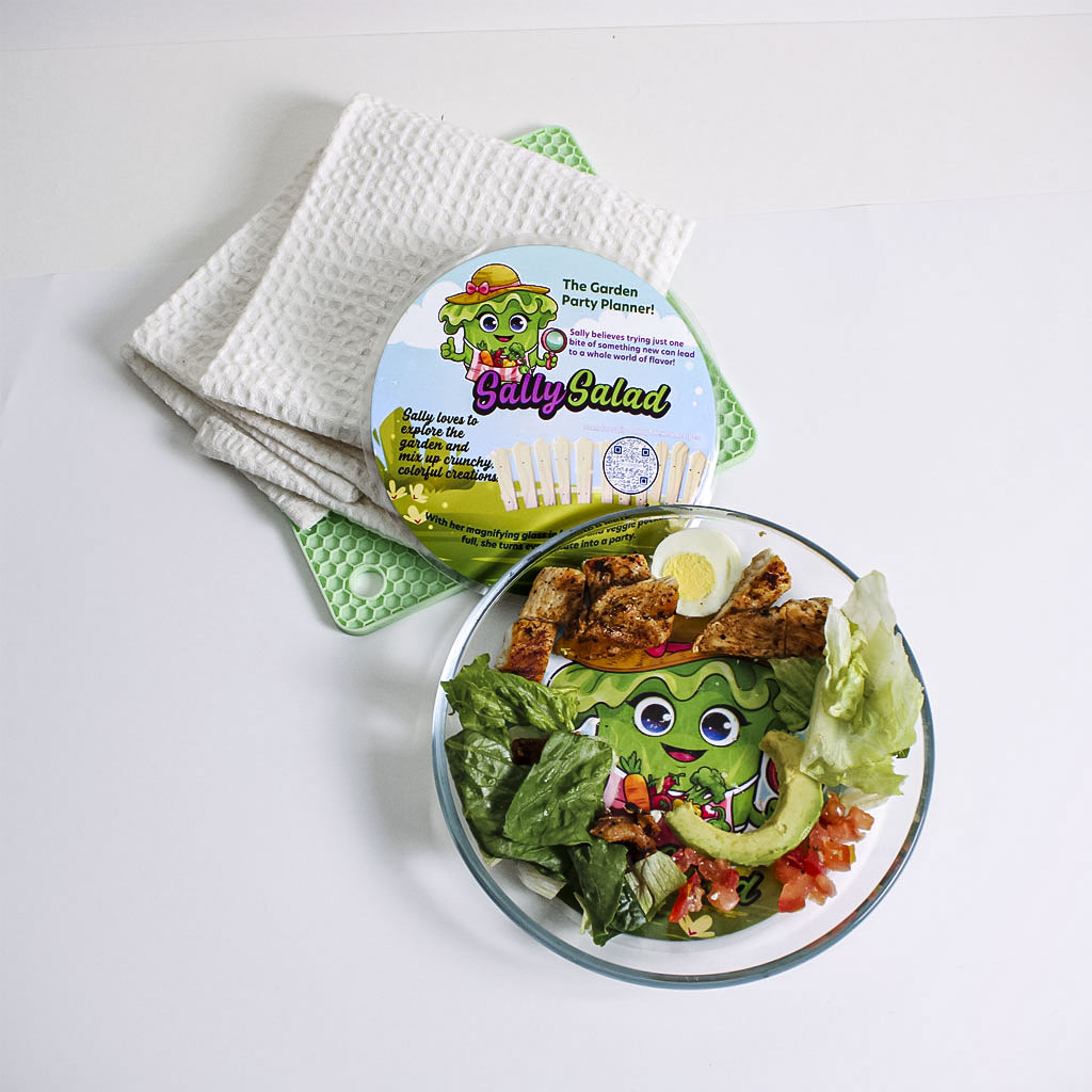 Sally Salad interactive kids plate with character mat under a clear plate topped with chicken and veggies, showing the Plate Buddies mealtime system in use.Sally Salad interactive kids plate with character mat under a clear plate topped with chicken and ve