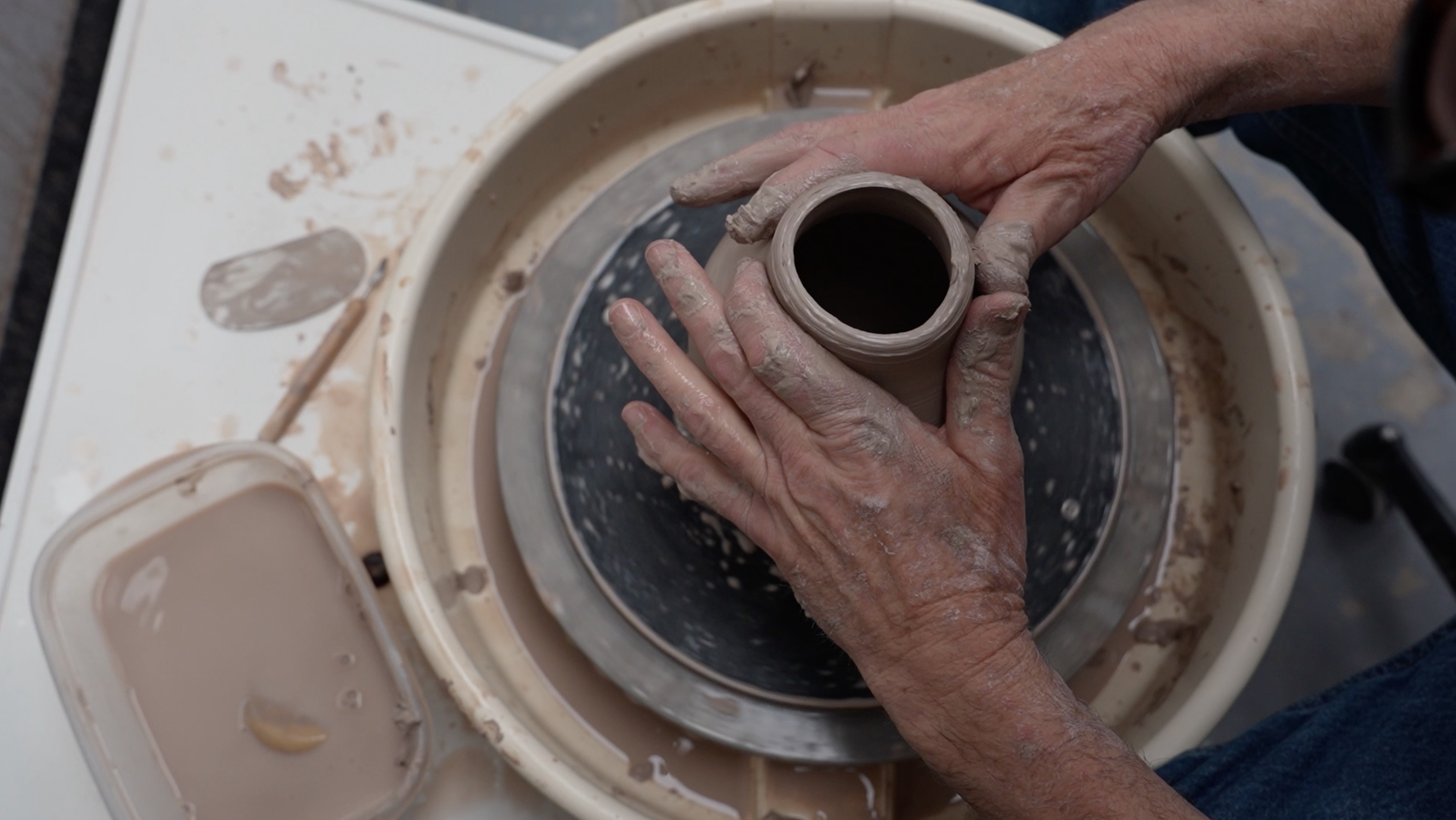 Hands shaping a vase on a pottery wheel with wet clay.