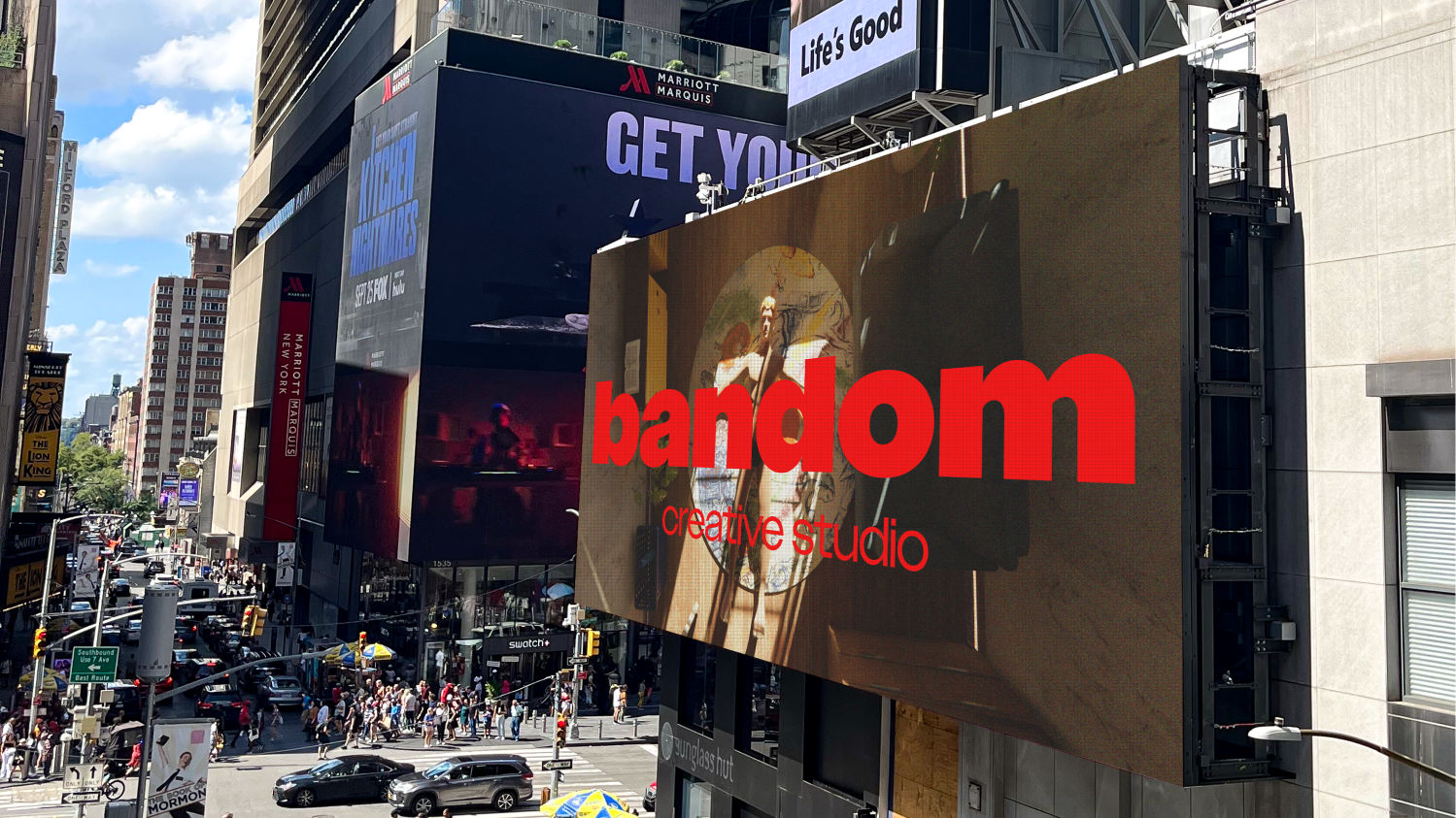 Large digital billboard in a busy city street displaying 'bandom creative studio' over an artistic image of a person in front of a decorative background.