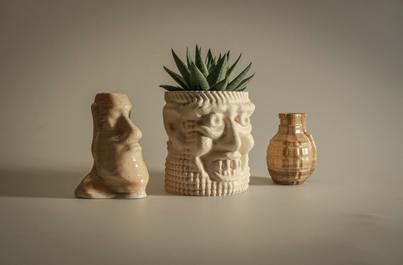 Three ceramic vases with textured surfaces; the middle one has a face design and contains a green succulent plant.