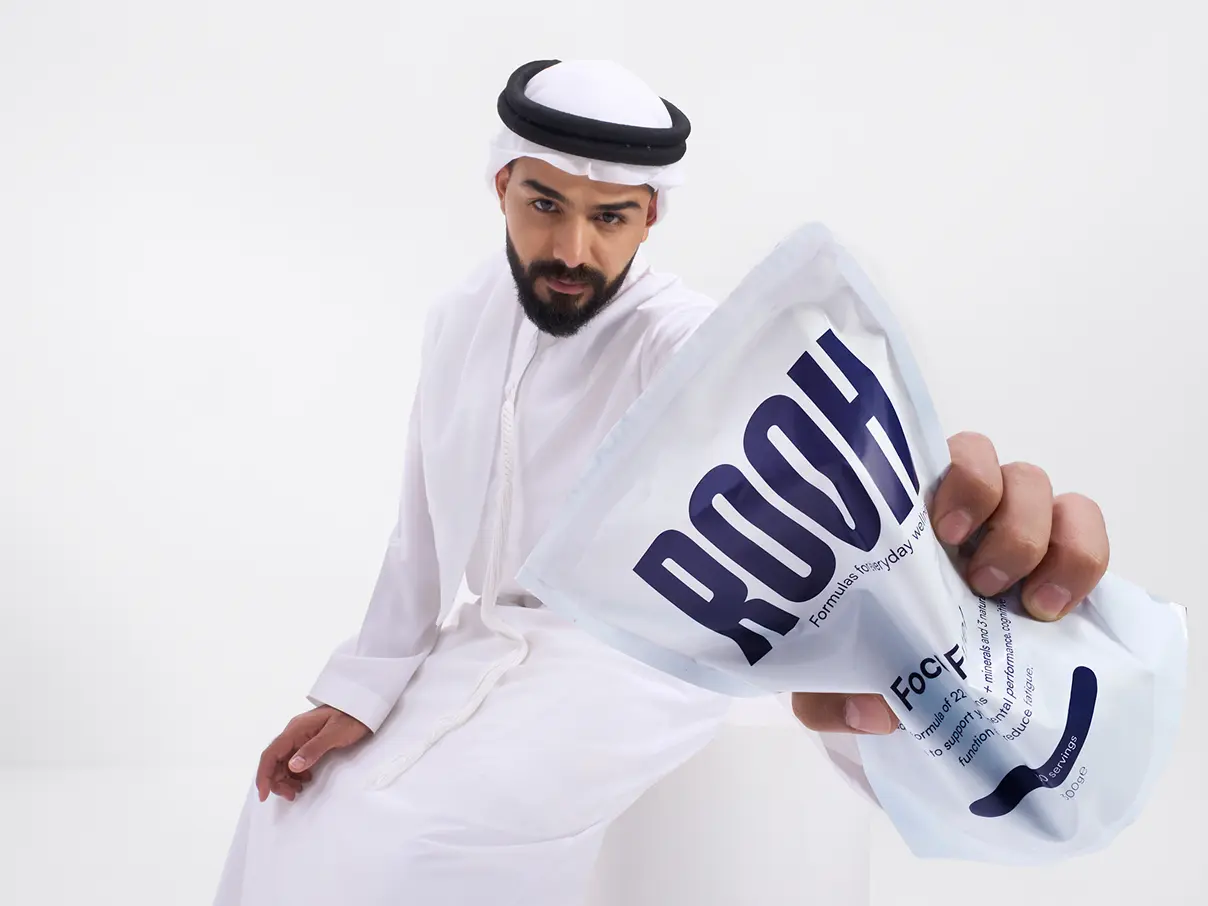 Male model wearing traditional Arabic clothing, posing for the camera and holding a ROOH formula bag.