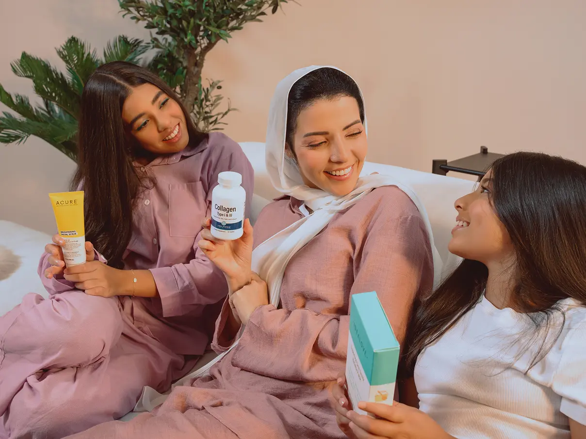 3 women sitting on a sofa, each holding an iHerb product.
