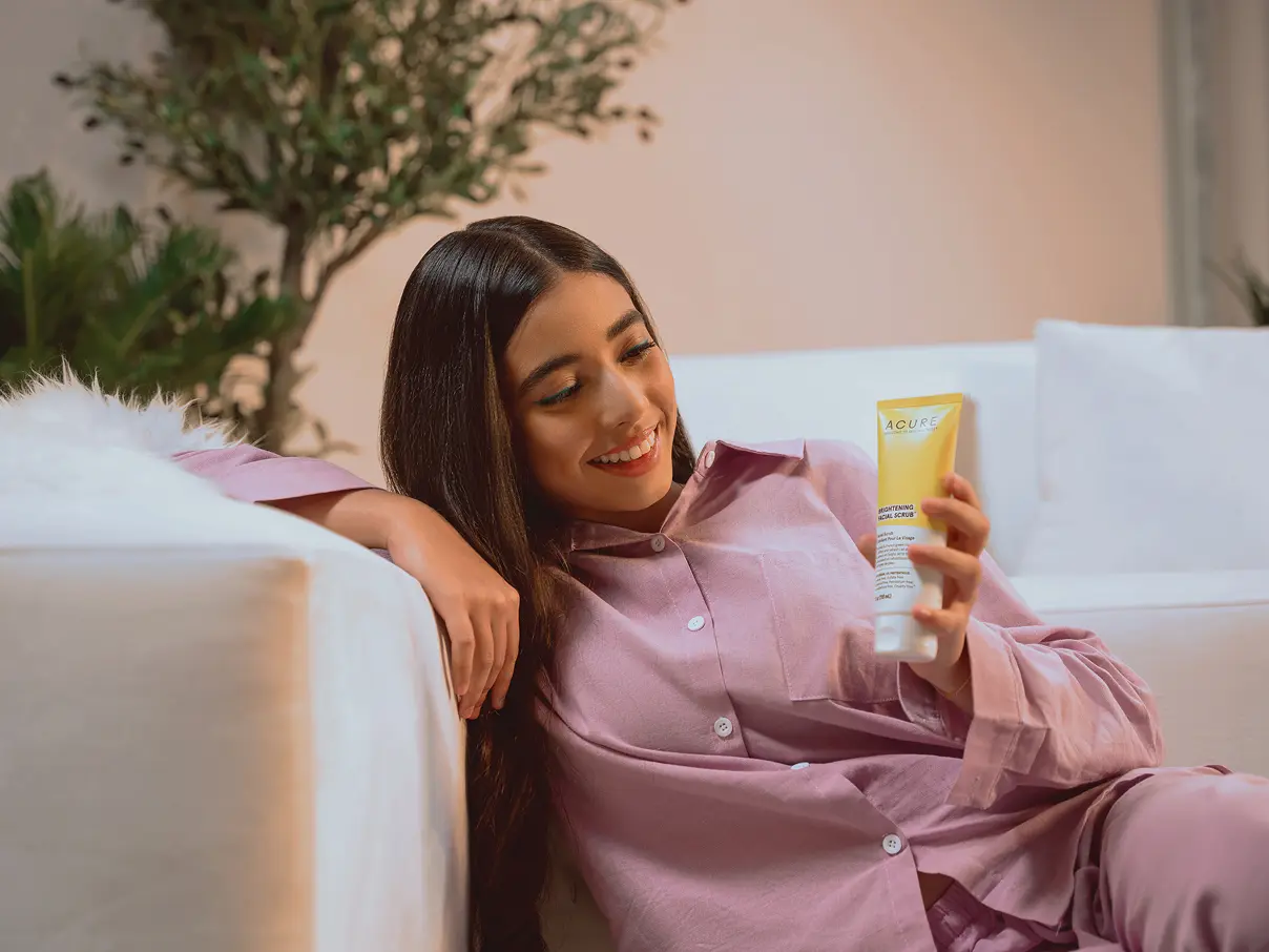 Woman sitting a white sofa, holding an iHerb product.