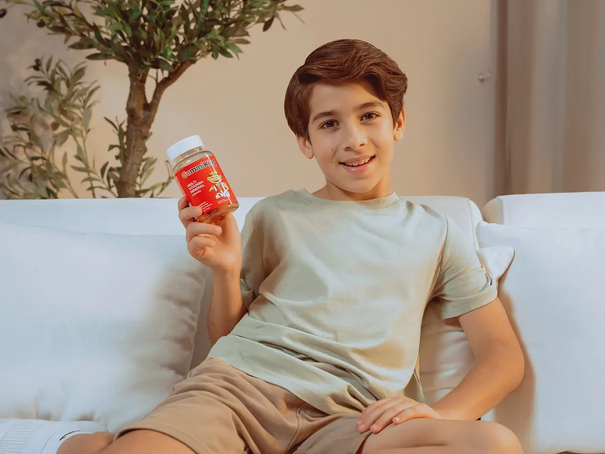 A boy sitting on a white sofa, holding an iHerb product.