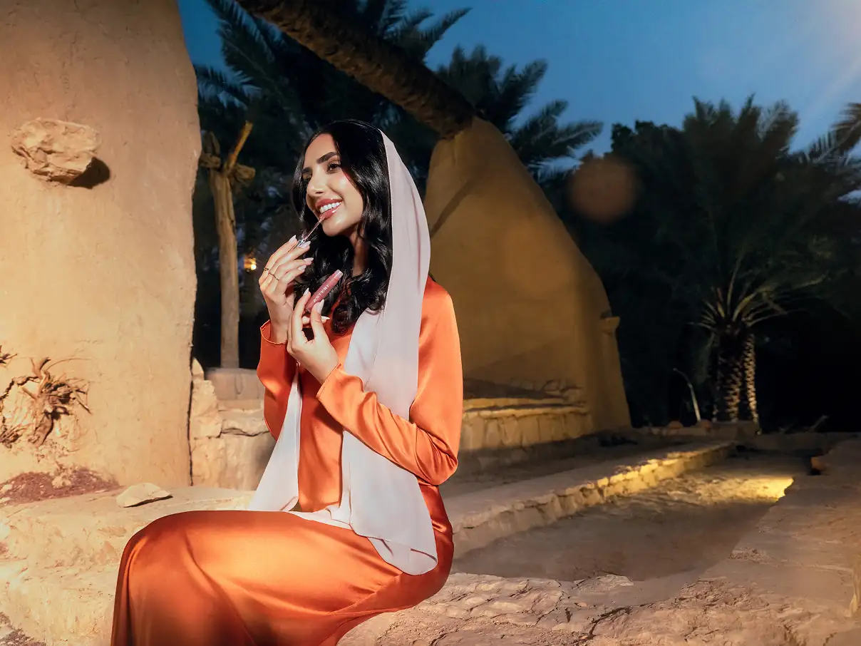 Female model, sitting outside applying lipstick.