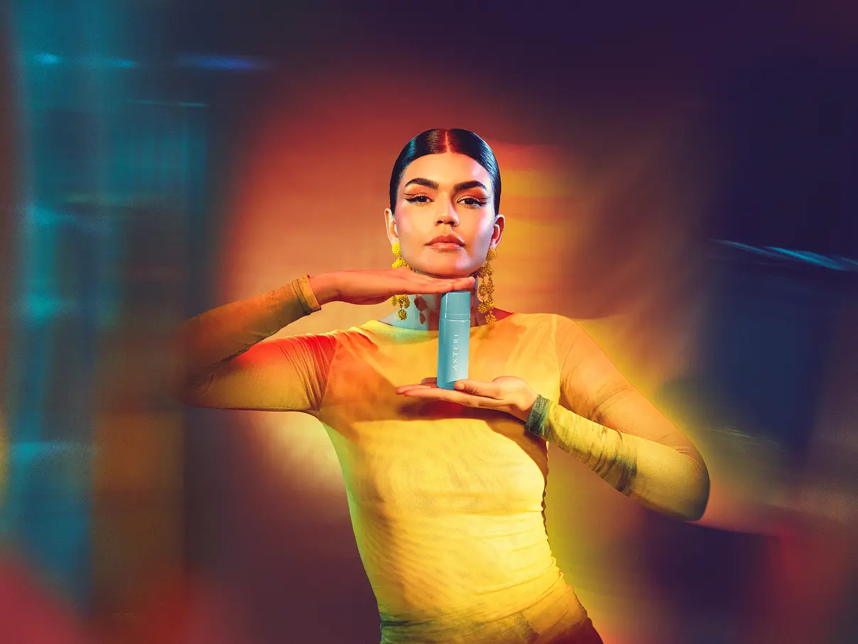 Female model posing holding an Asteri dessert mist bottle, blurred photo.