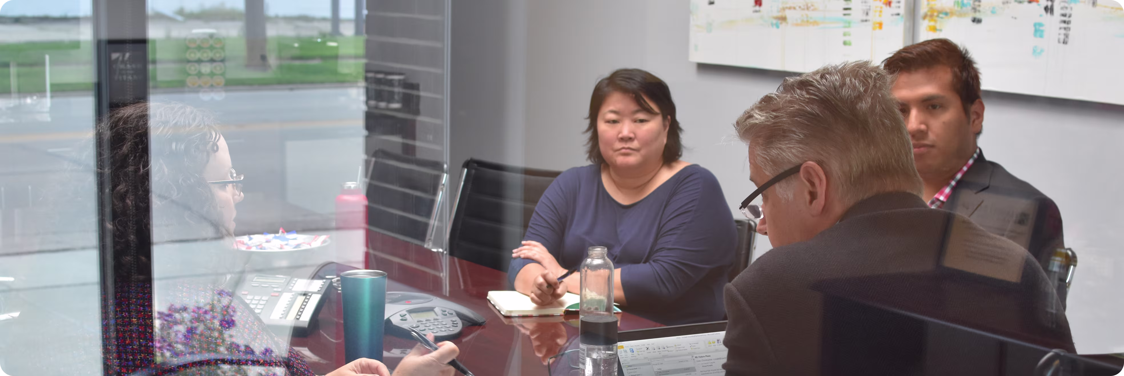 Four people having a meeting around a conference table with laptops, notebooks, and drinks.