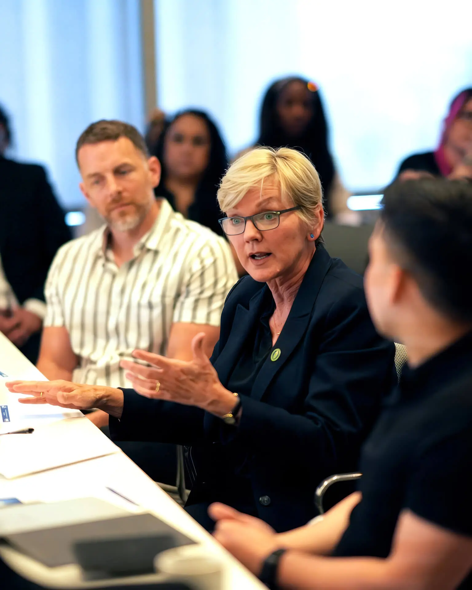 Former Secretary of Energy Jennifer Granholm speaking at meeting table surrounded by multiple attendees in background at Grounded Clean Energy Summit