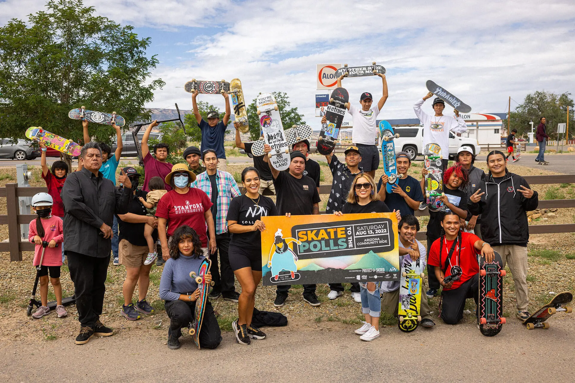Large group of Native American skateboarders holding skateboards and 'Skate to the Polls' banner at outdoor community event promoting voter participation through skateboarding culture
