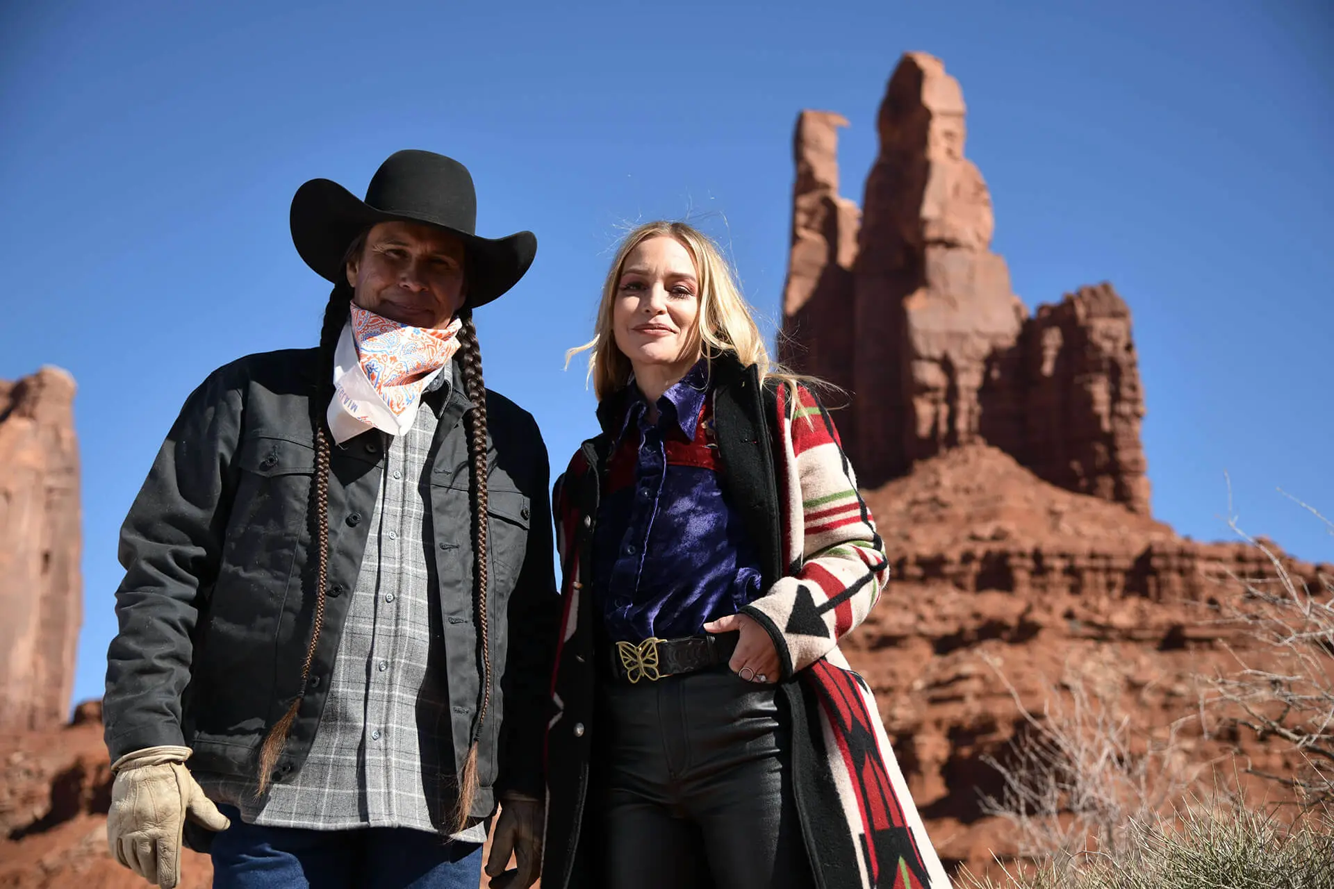 Actress Piper Perabo with Native American man in traditional black hat and braids standing together in desert landscape with red rock formations for Ride to the Polls campaign encouraging Native voting