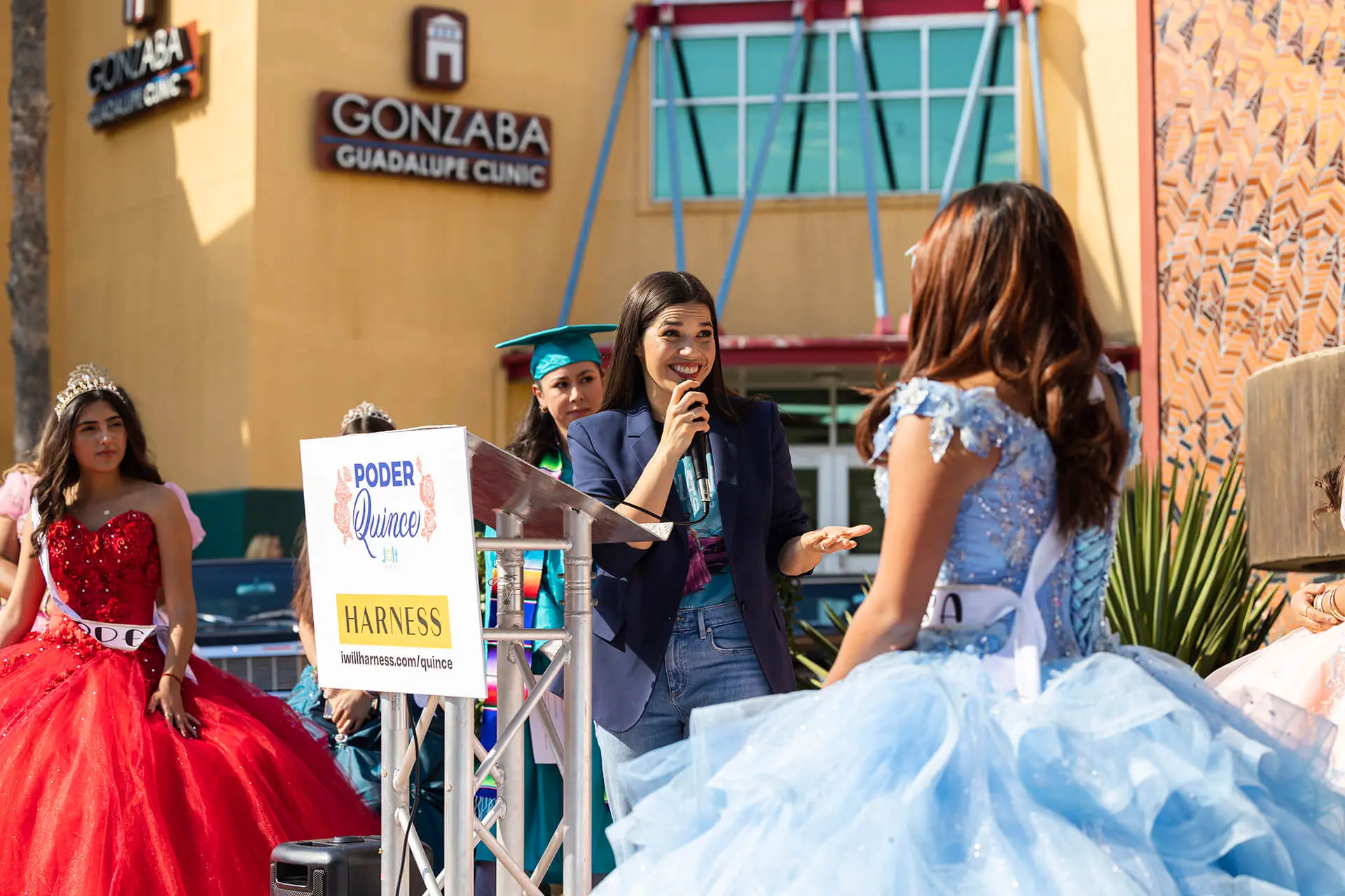 America Ferrera speaking at podium, addressing young women in formal quinceañera dresses at outdoor community event for Ride to the Polls voting campaign