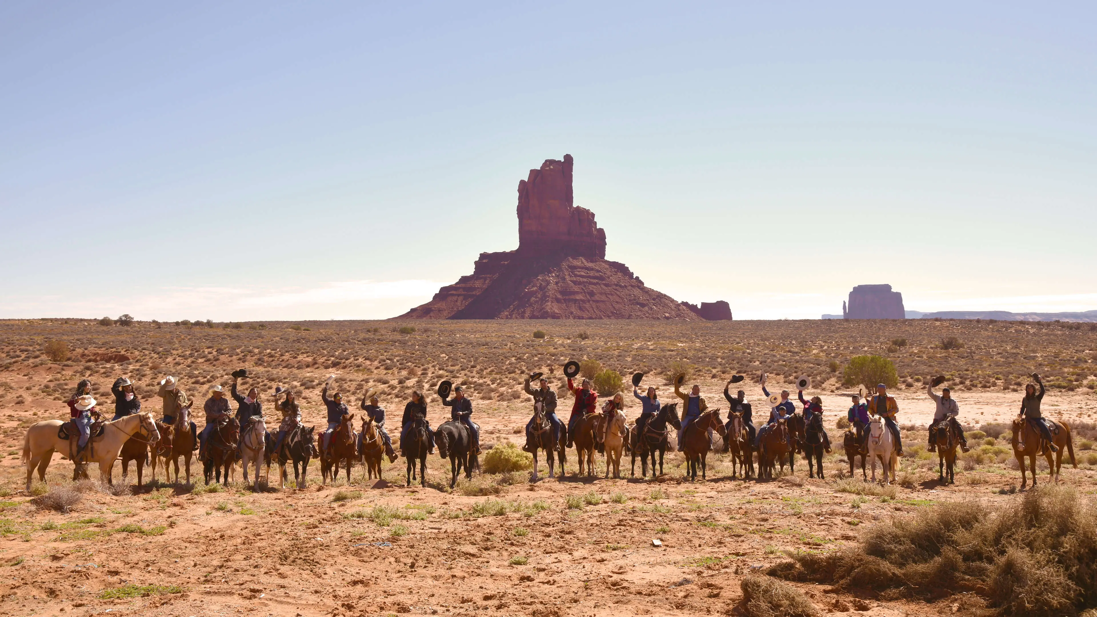 Large group of horseback riders spread across desert landscape with dramatic red rock formation in background for Ride to the Polls campaign honoring Native American voting traditions