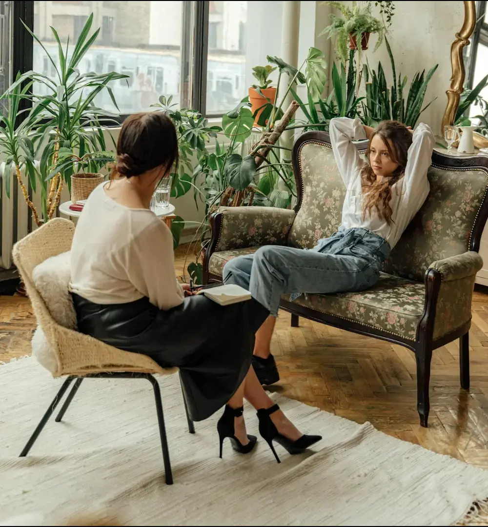 Therapist speaking with a patient during a mental health counseling session in a calm, plant-filled office setting.