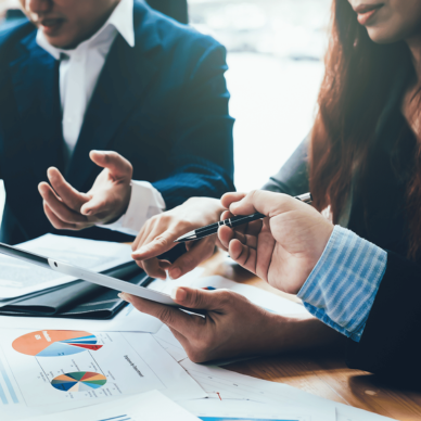 Three business professionals collaborating over charts and documents at a wooden table.