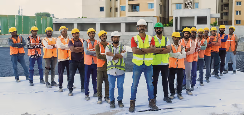 Group of construction workers wearing safety helmets and vests standing on a building site with arms crossed.