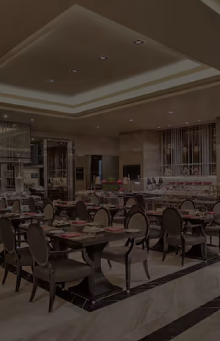 Elegant dining area with dark wood tables, cushioned chairs, and pink napkins in a modern restaurant.