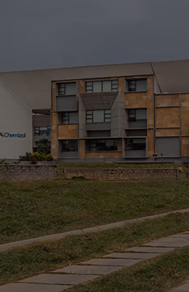 Modern industrial building with large windows, beige and gray panels, adjacent to a green grassy area with a stone pathway.